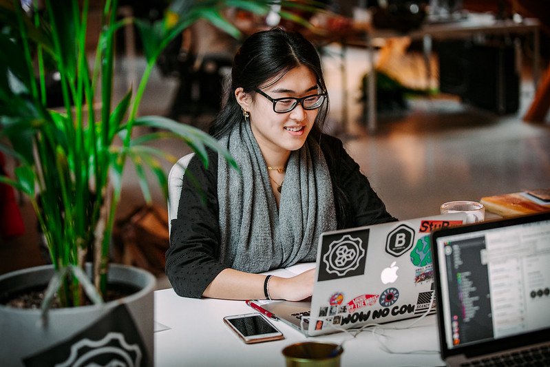A smiling woman sits in front of laptop emblazoned with a MozFest sticker.