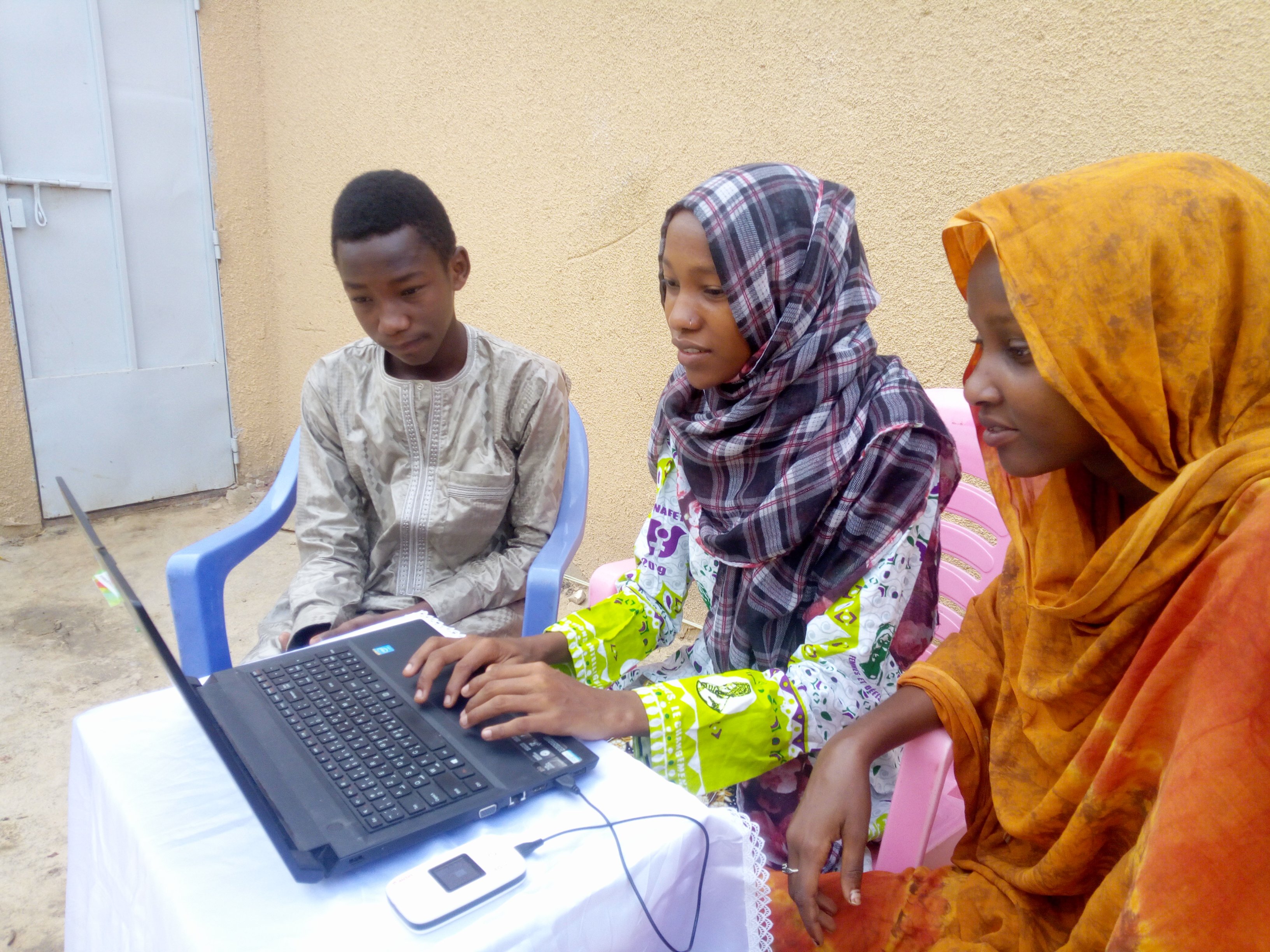 Chamsa Al Marif Nime, a Digital Grassroots Ambassador from Chad, sits with two other young people as they use a computer connected to a mobile internet modem