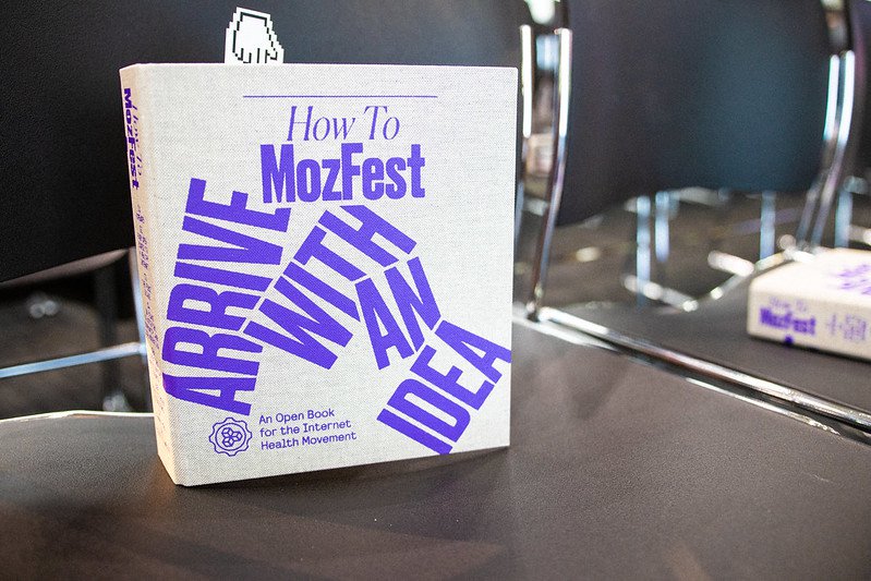 A photo of a book sitting upright on a chair. Cover reads "How To MozFest Arrive With An Idea"