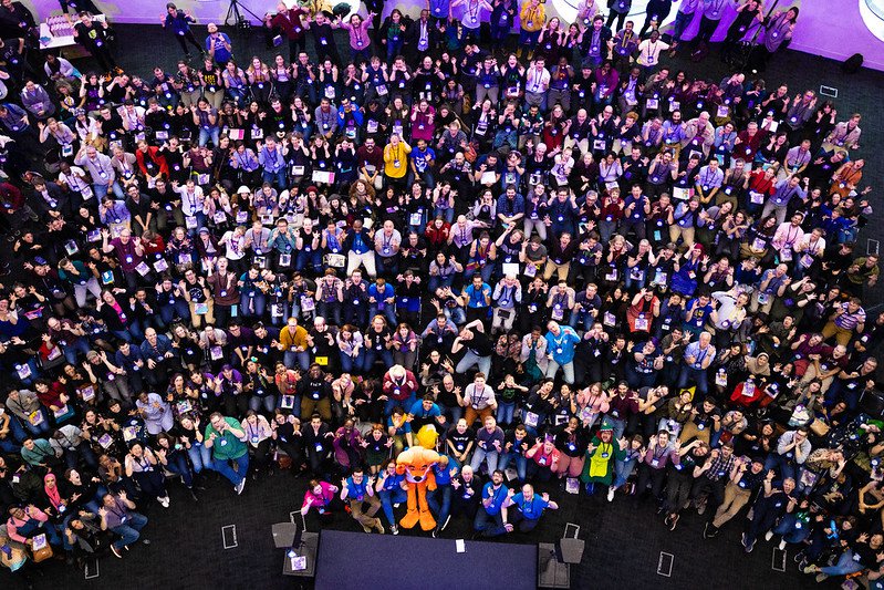 Camera is looking down on a large crowd of people who are making silly faces up at the camera