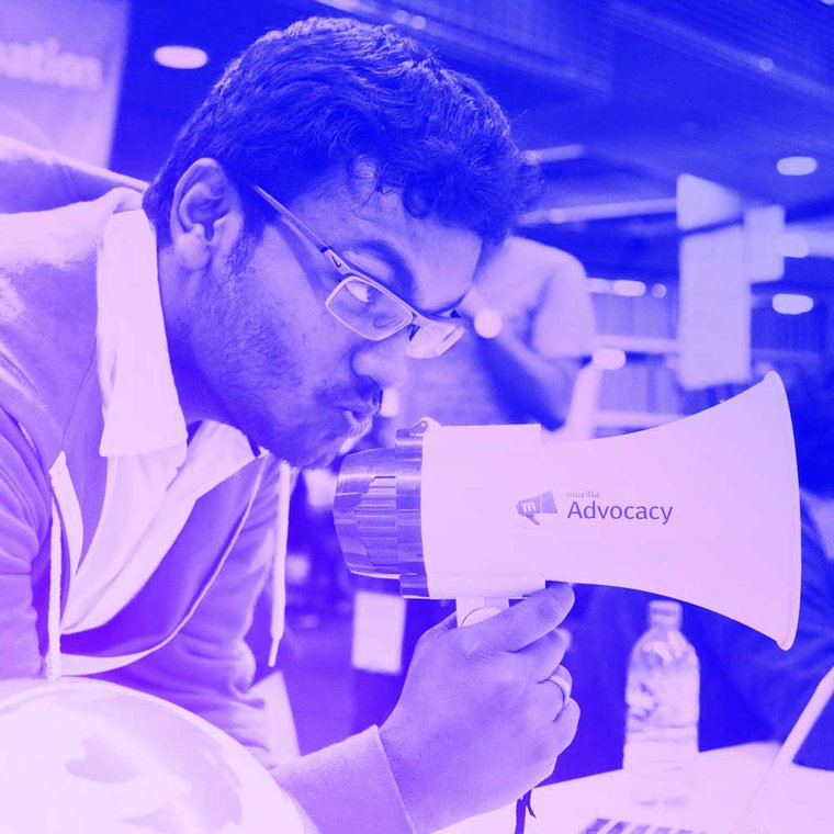 A person holds a megaphone, with a sticker that says 'Mozilla Advocacy', to their mouth.