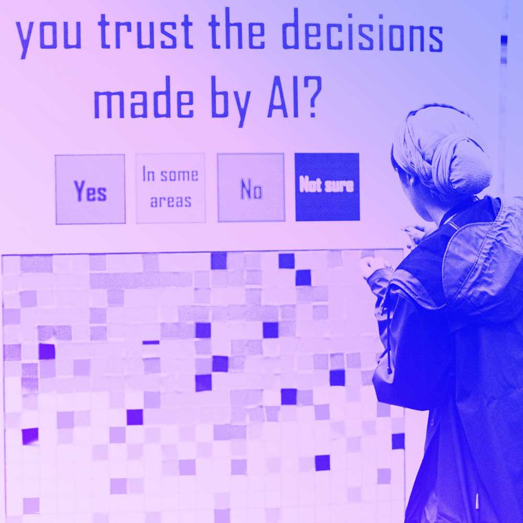 A person stands by an installation at MozFest with the title 'Would you trust decisions made by AI' with people adding red, yellow and green stickers depending on their level of trust.